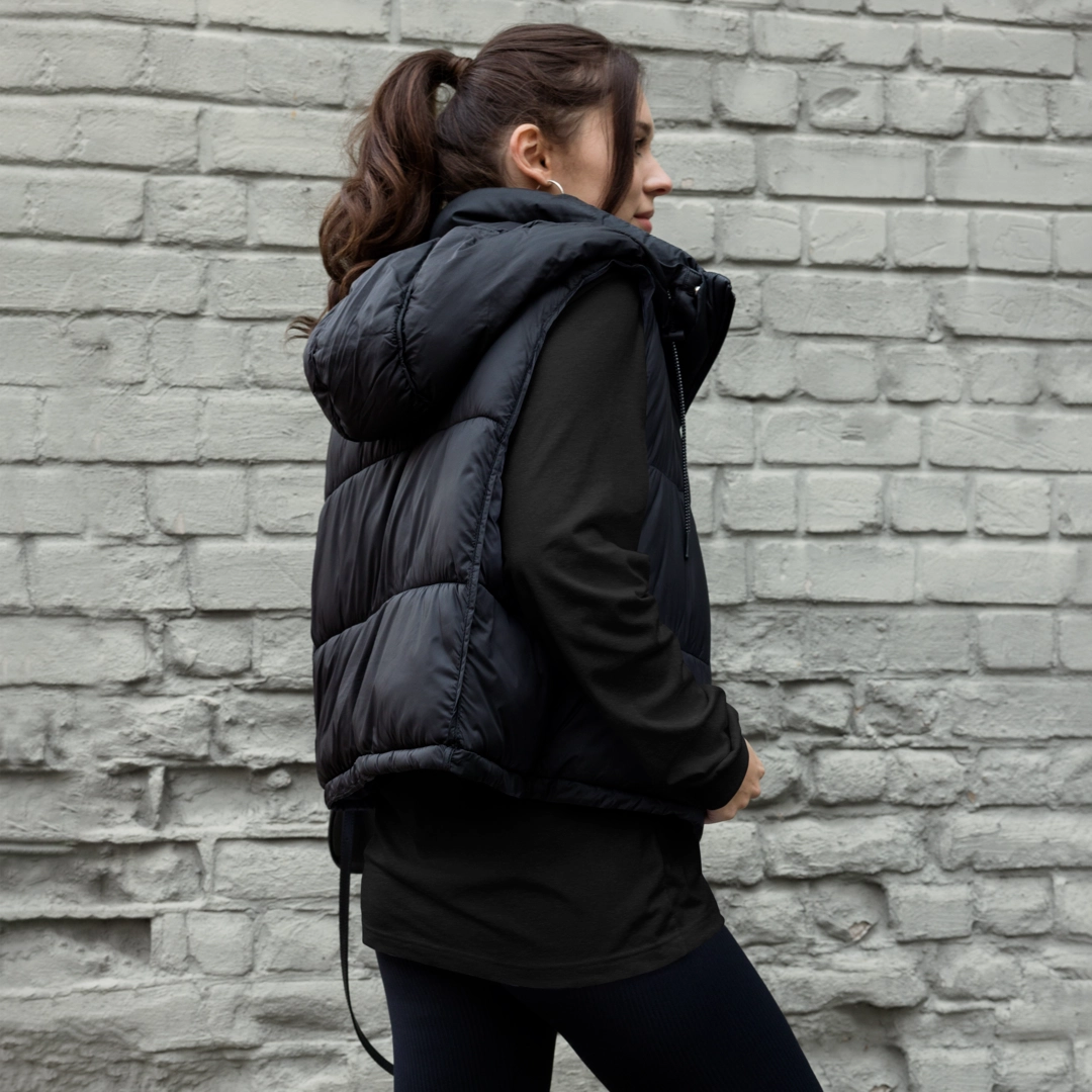 Side view of a woman wearing a dark gray YOLO-Chicago Flag Long Sleeve Crew T-Shirt paired with a black puffer vest.